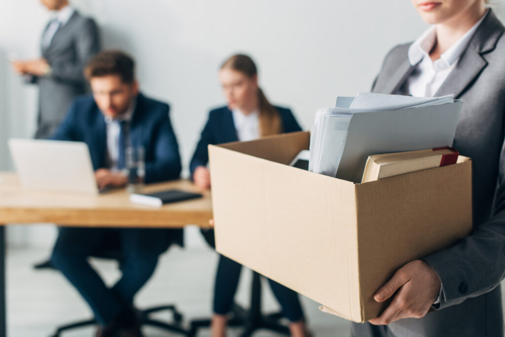Selective focus of fired woman holding cardboard box with book and papers in office